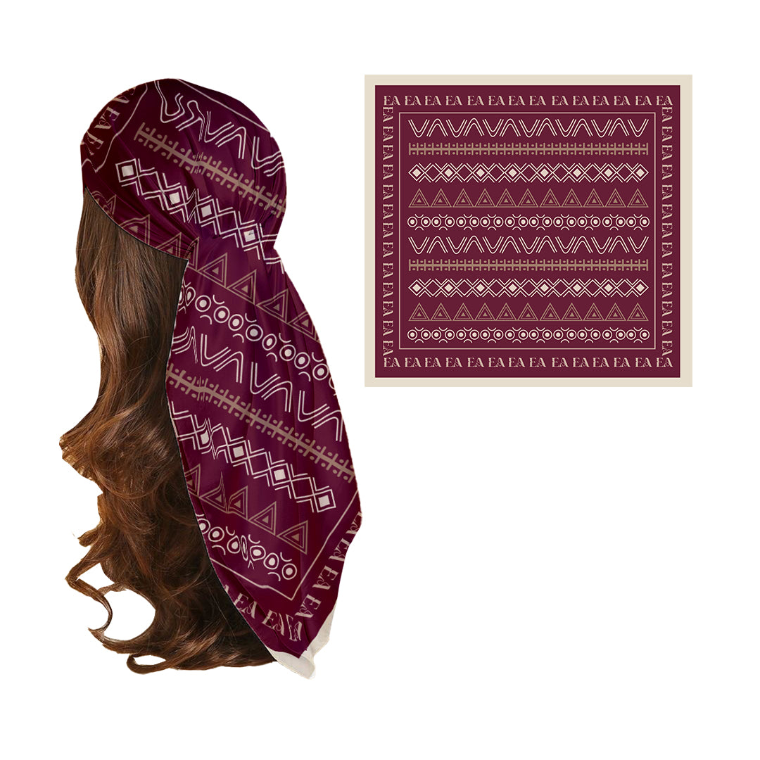 A silk head scarf with bold, striking African-inspired prints in rich burgundy tones, displayed on a mannequin with a close-up inset showing the fabric detail.
